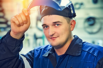 Portrait of Metal Locksmith. Young Caucasian man looks into camera from under visor of protective...