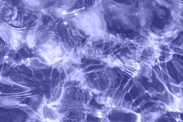 Very peri rippled water surface of swimming pool. Background of water repainted in trendy very peri color of the year 2022. Summer holidays, vacations resort concept. Full frame texture, top view.