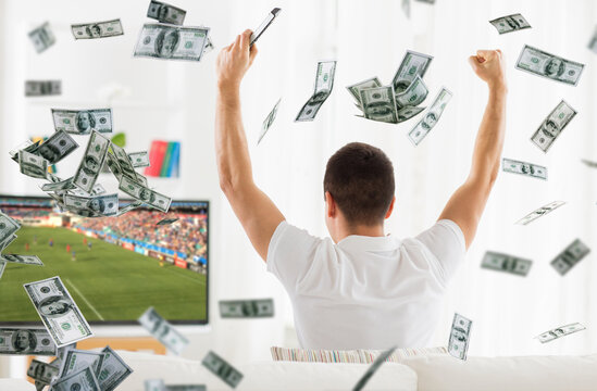 online betting, gambling and sport concept - happy man watching soccer game on tv with raised fists over money rain