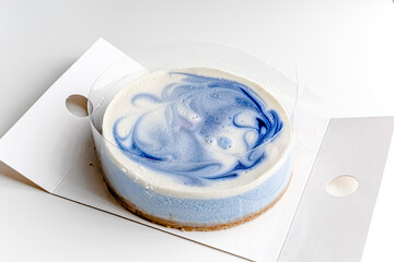 Piece of blue and white cheesecake with blueberry, cherry and black currant sauce inside on white plate on white table