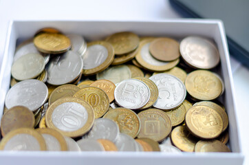 The sign of the Russian ruble on one of the coins and other iron coins in a white box. The concept of finance, investment, savings and cash.
