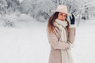 Fototapeta na wymiar Winter female fashion. Portrait of stylish young woman in snowy winter park wearing white and beige warm clothes