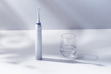 Electric toothbrush and  glass of water on toned  background with hard light and shadow. Modern...