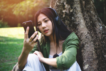 girl enjoy listening music with headphone,lady sitting under the tree in the park,summer time,Asian woman