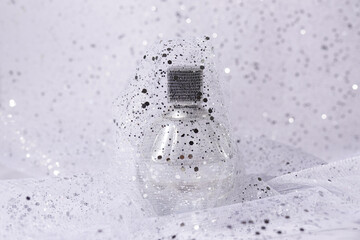glass perfume bottle with silver sequins on light background