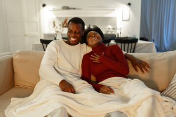 Fototapeta premium Happy black american couple laughing and having fun while relaxing together on sofa on weekend evening, overjoyed african man and woman close friends watching comedy on TV together, selective focus