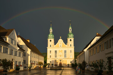 Arlesheim Cathedral after a thunderstorm. The sky is dark with a rainbow, the evening sun is illuminating the cathedral. Arlesheim, Basel, Switzerland.