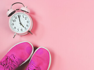 flat lay of pink sneakers and pink vintage alarm clock 5 o'clock on pink background with copy...