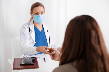 Young brunette woman having consultation at doctor office during coronavirus and flu outbreak. Female doctor wearing facemask, giving to patient jar with pills. Virus protection. Covid 19.