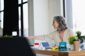 Side view of businesswoman working near models of houses and blueprints in office.