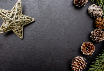 Fototapeta premium Christmas tree branches, cones and gold shiny star on the black stone plate as background. Holiday concept. Flat lay. Flat lay