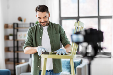 blogging, furniture restoration and home improvement concept - happy smiling man or blogger with camera sanding old wooden chair with sponge and recording tutorial video