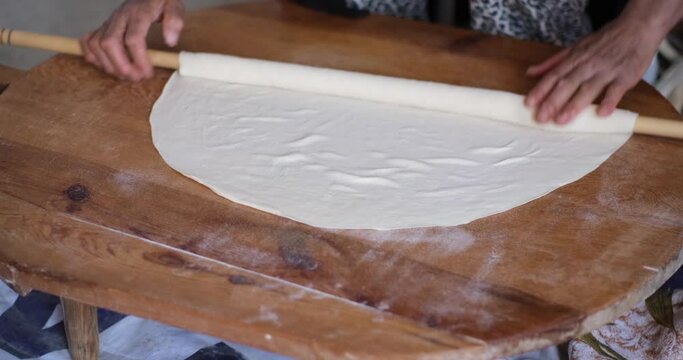 Female Hands Of Baker Rolls Dough In Flour On Wooden Board On Table With A Rolling Pin, In Bakery Shop, Woman Making Pizza Using Traditional Recipe At Home.