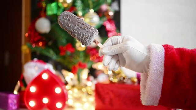 Santa Claus lifting up a fresh chocolate popsicle in front of Christmas decorations at home