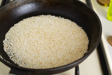 Sesame is fried in a cast iron pan in the home kitchen. The preparation process for the traditional Tahini sauce. Levantine cuisine concept.