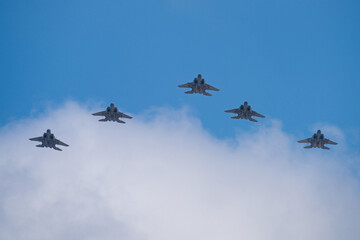 Five fighter aircrafts in v-formation with blue sky and white clouds.