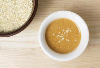 Tahini in a white bowl with sesame seeds in a brown bowl on a wooden background. Traditional Asian sauce for making hummus. Levantine cuisine concept. Horizontal orientation.