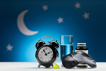 sleep disorder and medicine concept - close up of alarm clock, eye mask, glass of water, earplugs...