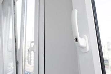 Opened white plastic window handle in upright position close-up. New tilt and turn pvc windows ventilation.