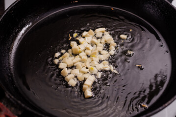 Garlic is fried in oil in a cast-iron frying pan. The process of cooking vegetarian food.