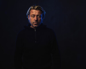 Shadowy night portrait of a man with blond hair a stubble and a black woolen sweater.