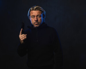 Shadowy night portrait of a confident man with a gun in his hand with blond hair, a stubble beard and a black wool sweater.