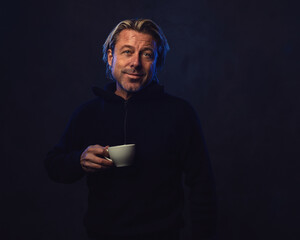 Shadowy night portrait of a happy smiling man with a white cup of coffee in his hand with blond...