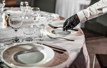 Waitress hand in gloves puts the knife and fork, table setting