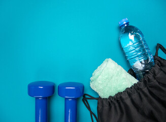 Two heavy dumbbells and a training bag with towel and plastic bottle of water. Healthy fitness lifestyle composition. Gym flat lay concept with copy space on blue background.