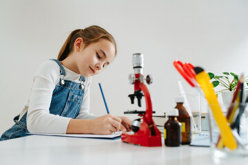 Diligent little girl trying to do science project, writing dow her observations