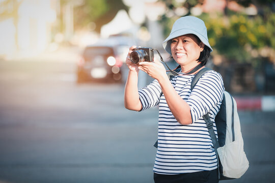 Asian woman traveling and taking pictures outdoors city streets,
Asian female happy smiling backpacker using camera to take image on city walk streets, business travel concept.