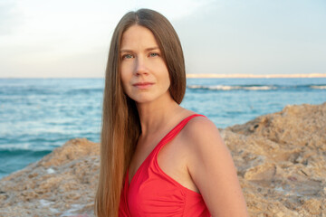 Portrait of a beautiful middle-aged girl with long hair in a red dress on the seashore.