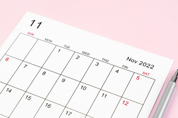 November 2022 calendar sheet with pen on pink background.