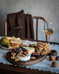 Appetizer. A glass of white wine, grapes, figs, pear, nuts and honey on a black wooden board. Dor...