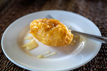 Deep fried banana fritters topping with honey on the white plate on wooden table