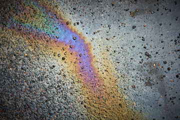 A spot of oil or gasoline in a puddle on the asphalt. Top view of asphalt with oil after rain