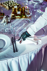 Waitress hand in gloves puts the knife and fork, table setting