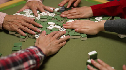 closeup view of hands mixing mahjong tiles on the table with green cloth. traditional asia gambling...