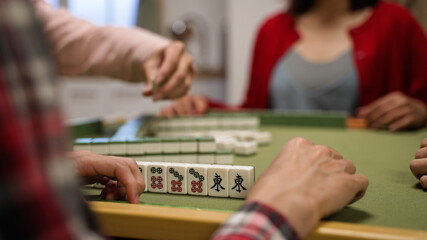 closeup with selective focus of a hand tapping on the table while waiting for his turn at gambling table. asian traditional strategy game concept. words on mahjong tile translation: east - obrazy, fototapety, plakaty