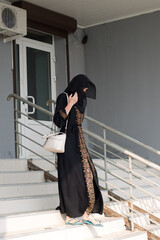 woman in black Muslim dressy clothes in burqa comes out of her house into the street.