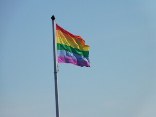 A colorful Pride rainbow flag in the wind with blue sky 