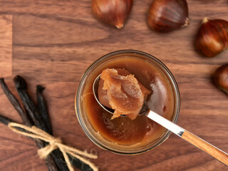 A jar of vanilla chestnut spread, with a spoon, chestnuts, and vanilla pods, on a walnut table, top...