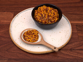 A bowl of french mustard, with a spoon, on a walnut table