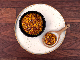 A bowl of french mustard, with a spoon, on a walnut table, top view