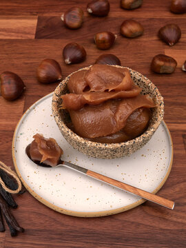 A bowl of vanilla chestnut spread, with a spoon, chestnuts, and vanilla pods, on a walnut table