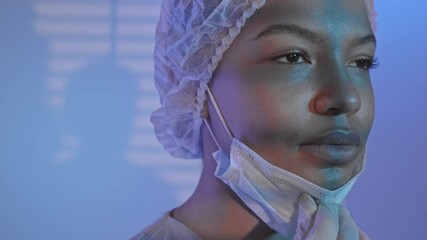 Tilt closeup slowmo portrait of tired biracial female surgeon taking off face mask and wiping sweat after surgical operation