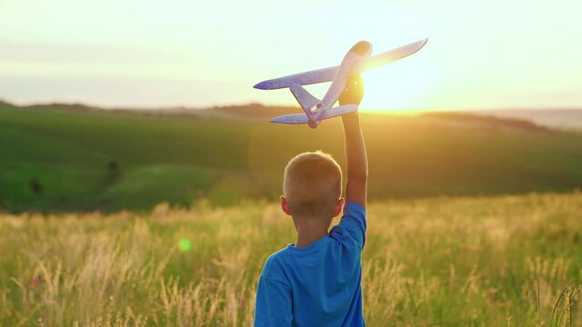 A boy plays with a toy plane, on the field in the sun, wants to become an astronaut. The concept of a free childhood dream. The kid plays with his favorite toy airplane, in the summer in the park