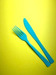 Plastic cutlery knife and fork turquoise teal blue on vivid  Yellow Bright background