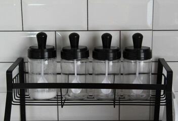 Glass jars stand in row on black steel shelf.