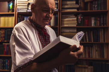 Senior man in folk clothes holding an book at home library